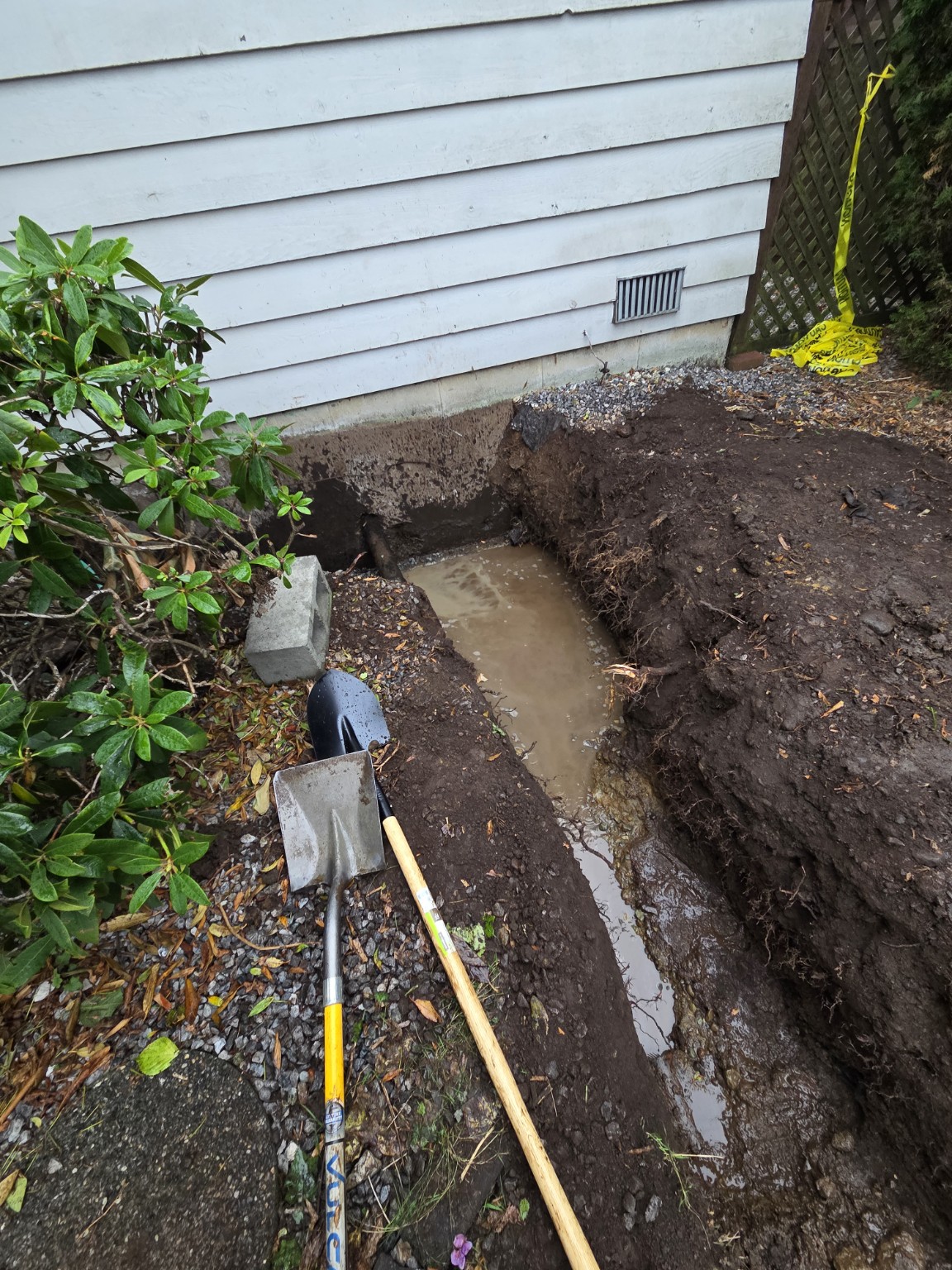 Excavated foundation drainage route with standing water and hand tools
