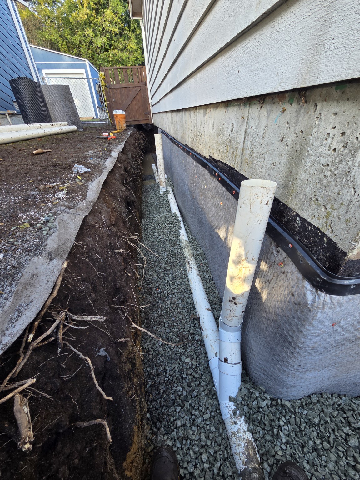Perimeter drain pipe and risers in aggregate beside a foundation membrane